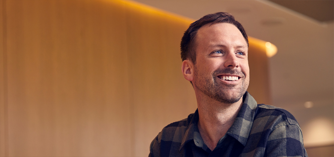 Jordan sentado y sonriendo con las manos entrelazadas frente a él.