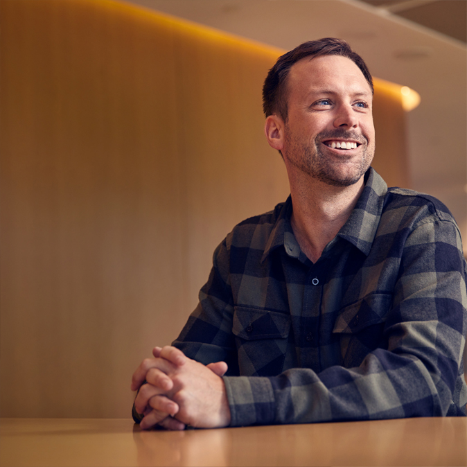 Jordan sentado y sonriendo con las manos entrelazadas frente a él.