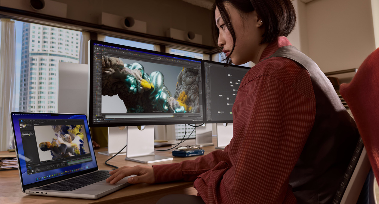 Eine Person in einem Büro arbeitet an einem MacBook Laptop, der über einen Thunderbolt 5 Anschluss mit einem Studio Display XDR verbunden ist