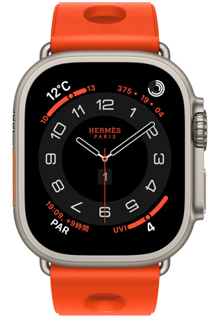 ナチュラルチタニウムケースのApple Watch Hermès Ultra 3。アナログデザインのCirculaire文字盤に、時針、分針、秒針と、天気、アクティビティリング、パリ時間、UV指数のコンプリケーションが表示されている。右側面の外観には、Digital Crown、少し突き出たサイドボタンが見えている。ラバー素材を成形し、中央に円形のカットアウトをあしらった、オランジュ・ネオン（ブライトオレンジ）のスキュブHダイビングストラップが付いている