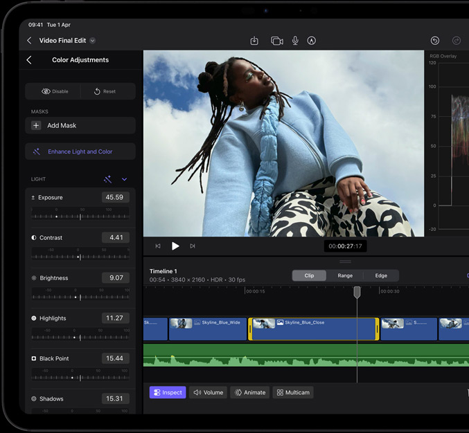 iPad Pro, front exterior, black display bezel, display showing video editing app with a picture of a model in a blue coat and black and white printed trousers, colour adjustment panel open on the left with various video effects and sliders, timeline at the bottom with multiple video clips and audio tracks