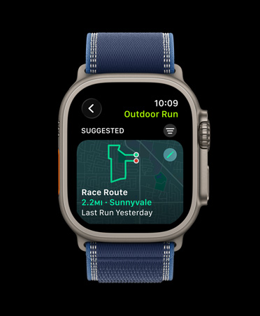 Apple Watch Ultra 3 med urkasse av naturlig titan og Trail Loop i blå/klarblå viser Løp en rute-funksjonen under løping utendørs.