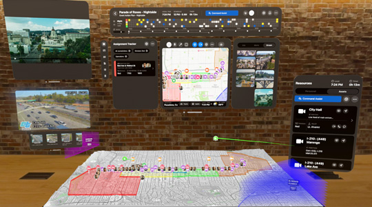 A 3D projection of dashboards for first responders shows camera feeds, team assignments, and a 3D map of a parade route, in front of a brick wall inside an office