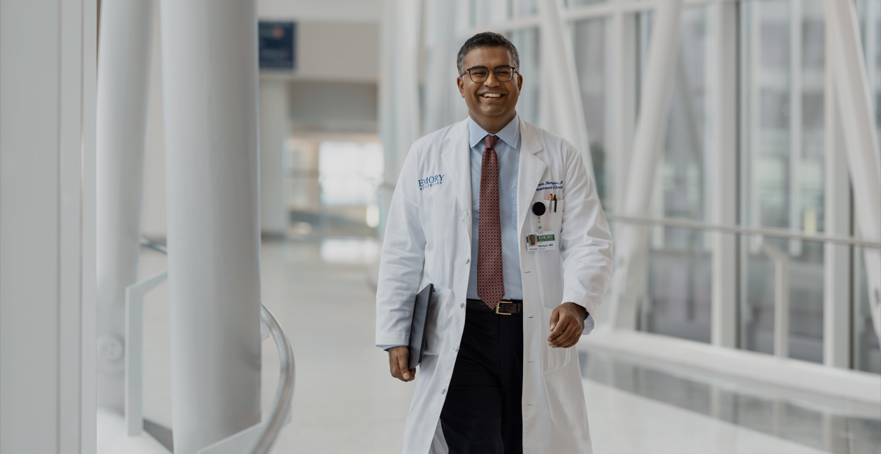 一個醫生正在行走，右手拿著一部 MacBook。 