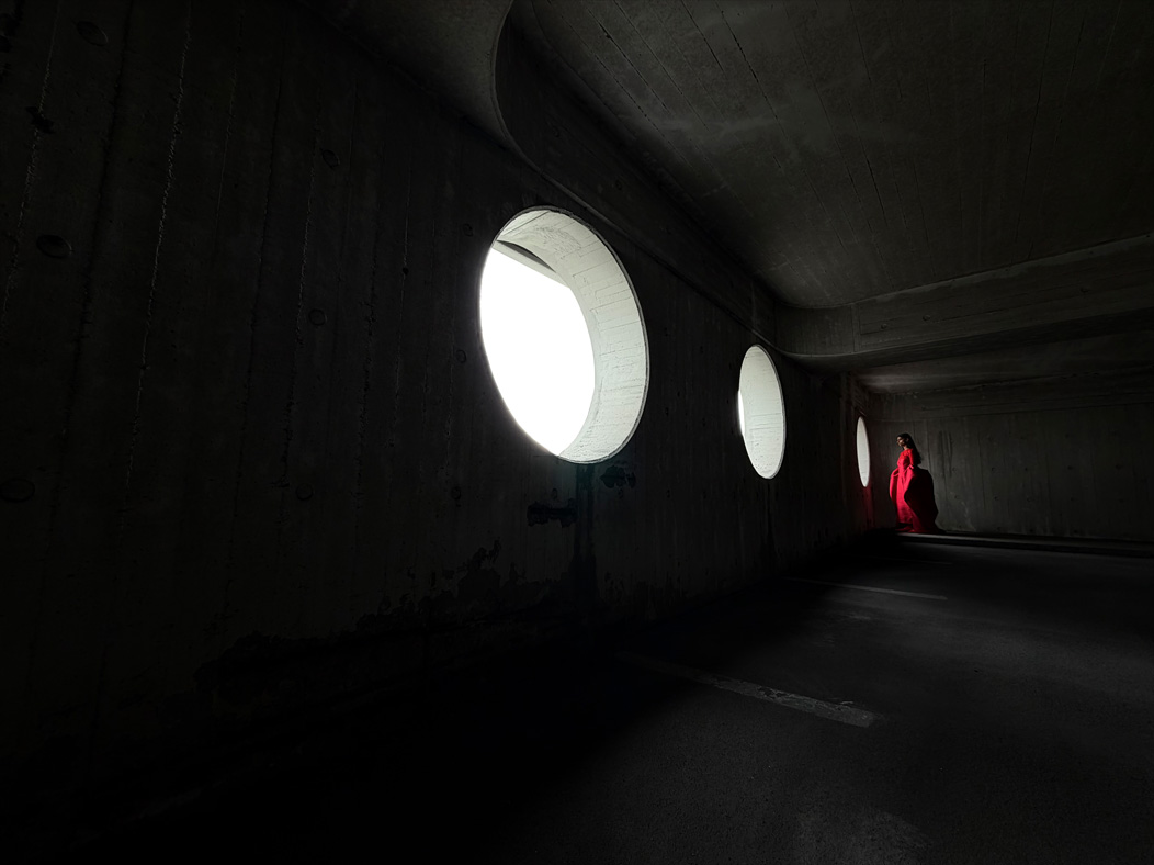 En kvinna i en lång röd klänning står i ett tomt rum och blir fotograferad. Appen Kamera växlar mellan olika brännvidder för att demonstrera möjligheterna med proffskamerasystemet, nu visas 13 mm